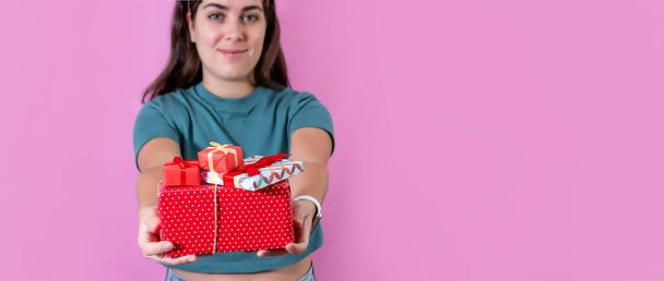 A girl holding gifts boxes over the pink background with a copy space - Фото, зображення