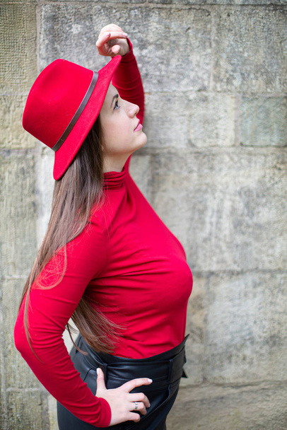 Looking up white woman with long dark hair in bright red near stone wall - Valokuva, kuva
