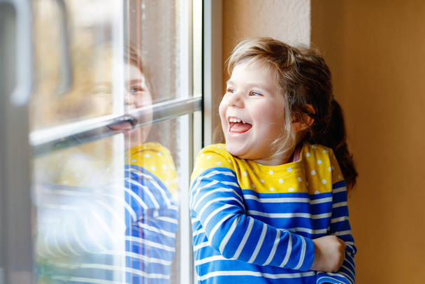 Cute little girl by window holding selfmade heart as gift for Valentines day, Mothers day or birthday. Adorable happy smiling child indoors. - Photo, Image