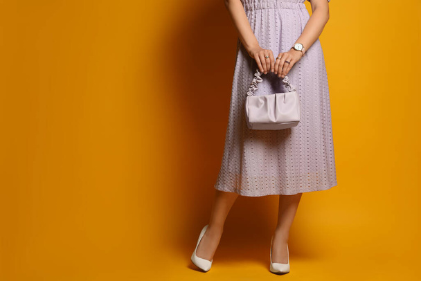 Fashionable woman with stylish bag on orange background, closeup. Space for text - Valokuva, kuva