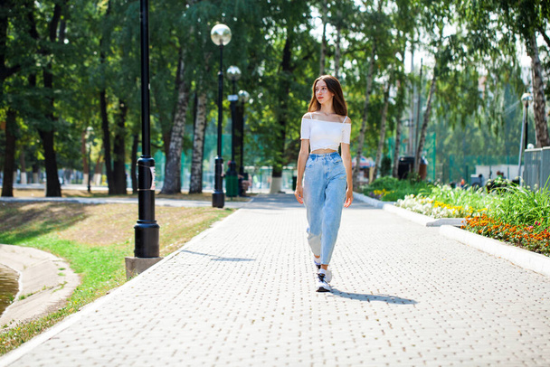 Full length portrait, young beautiful girl in blue jeans posing in a summer park - Фото, изображение