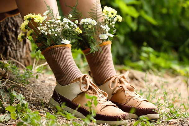 Woman sitting on stump with flowers in socks outdoors, closeup - Foto, immagini