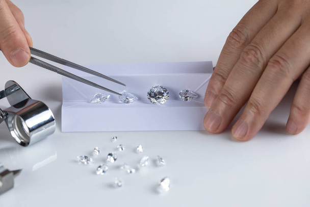 Close up of diamond experts hand at workplace evaluating gemstones polished diamonds. - Foto, afbeelding