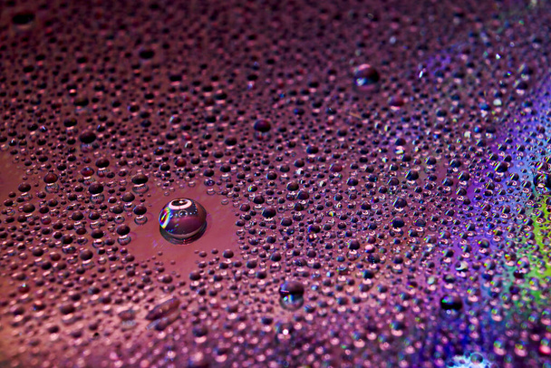 A selective focus shot of colorful reflective water drops on a digital disc surface. various RGB LED lights illuminate the scene. - Foto, afbeelding