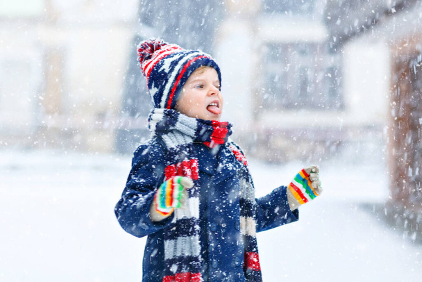 Cute little funny child in colorful winter fashion clothes having fun and playing with snow, outdoors during snowfall. Active outdoors leisure with children. Kid boy and toddler catching snowflakes. - Photo, Image