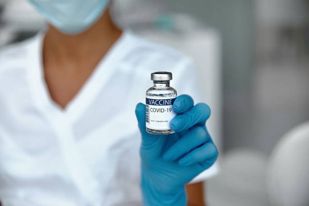 Coronavirus Vaccine in glass bottle in hand of doctor.  Vaccine jar on white background in blue glovs. Vaccine Concept of fight against coronavirus - Fotoğraf, Görsel