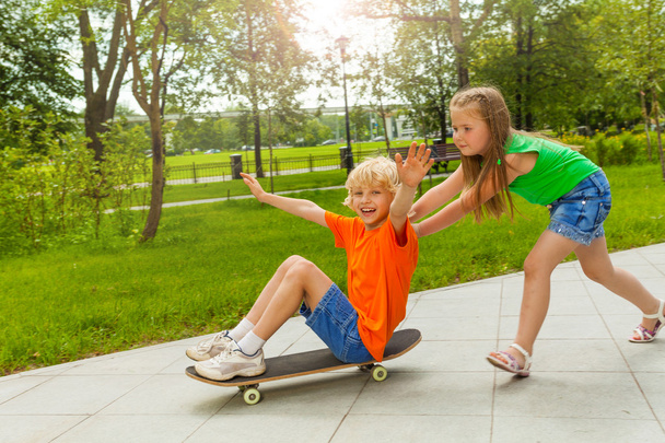 Girl pushes boy on skateboard - Фото, зображення