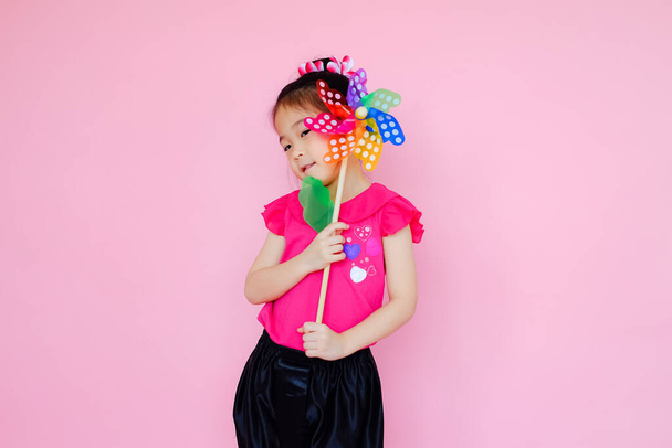 Little cute asian small girl on pink background with colorful wind turbine or pinwheel or wind toy - Фото, зображення