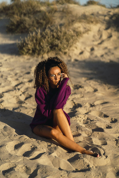 A vertical shot of an attractive female with tattoos and a cozy purple sweater walking on a beach - Photo, image