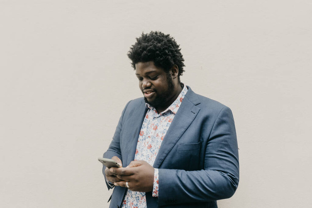 A shallow focus of a black man looking at his phone on a blank wall background - Foto, immagini