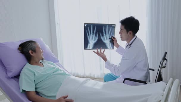 asiatico maschio medico tenendo mano osso x-ray film parlare con il maschio paziente spiegare il trattamento e dare incoraggiamento. - Filmati, video