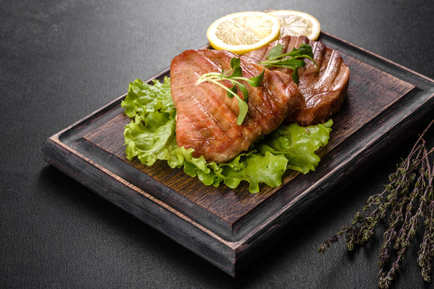 Вкусный сочный стейк из тунца, приготовленный на гриле со специями, травами и ломтиками лимона на тёмном фоне - Фото, изображение