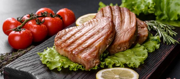 Köstliche saftige Thunfischsteak gegrillt mit Gewürzen und Kräutern und Zitronenscheiben auf dunklem Hintergrund - Foto, Bild