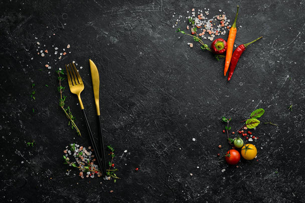 Cutlery on a black stone table with vegetables and spices. Food background. Top view. Rustic style. - Fotó, kép
