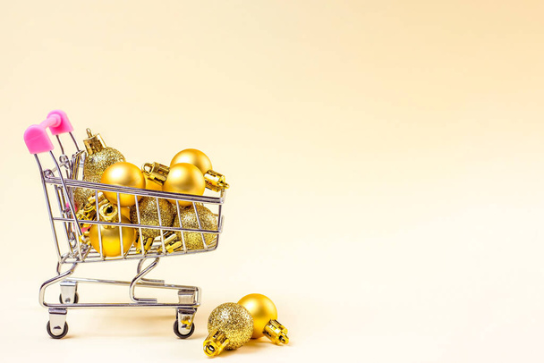 コピースペース付きの光の背景に金色のクリスマスの泡が付いているトロリーショッピングカート。クリスマスセール、割引、休日の買い物やプレゼントのコンセプト. - 写真・画像