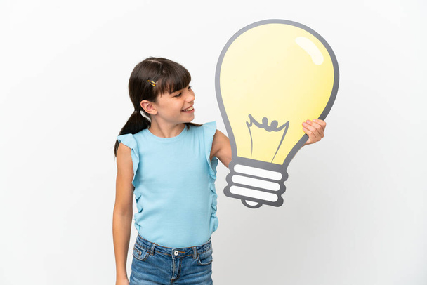 Little caucasian kid isolated on white background holding a bulb icon with happy expression - Foto, Imagen