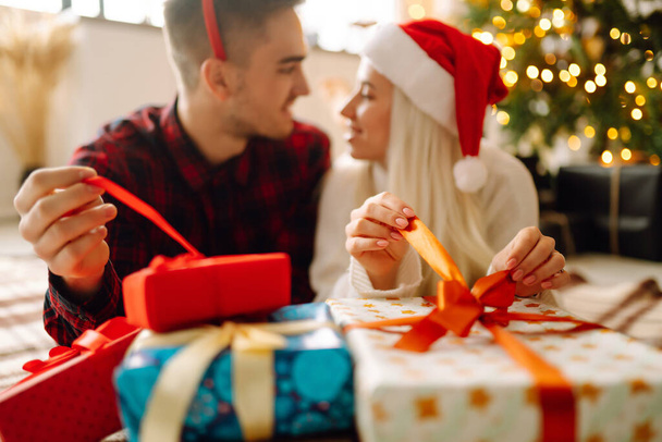 Cheerful young male and female Exchange of Christmas gifts. Young couple opening gift box near Christmas tree. Romantic day. Winter holidays. - Foto, Imagen