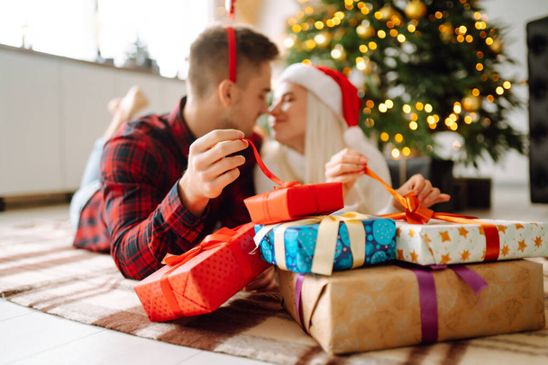 Cheerful young male and female Exchange of Christmas gifts. Young couple opening gift box near Christmas tree. Romantic day. Winter holidays. - 写真・画像