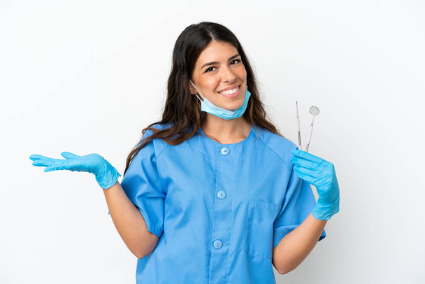 Mujer dentista sosteniendo herramientas sobre fondo blanco aislado con expresión facial impactada - Foto, Imagen