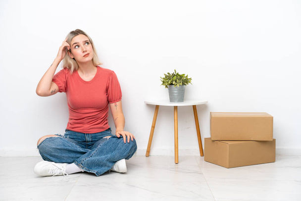 Mujer joven moviéndose en nuevo hogar entre cajas aisladas sobre fondo blanco teniendo dudas y con expresión de cara confusa - Foto, imagen