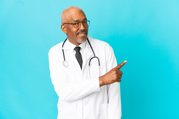 Senior arts man geïsoleerd op blauwe achtergrond wijzen terug - Foto, afbeelding