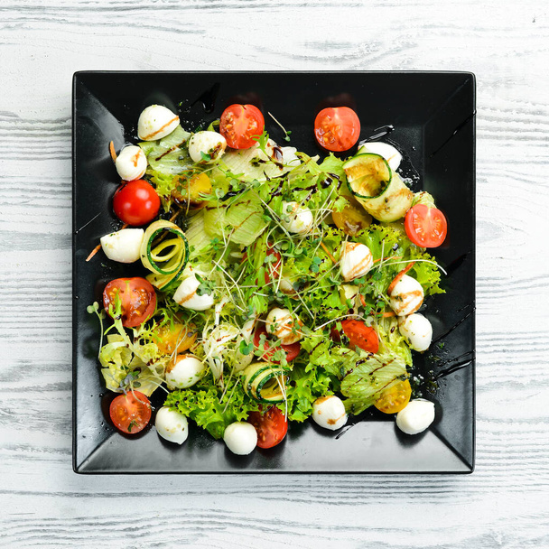Vegetable salad with mozzarella cheese. On a black plate. Top view. Food. Rustic style. - Photo, Image