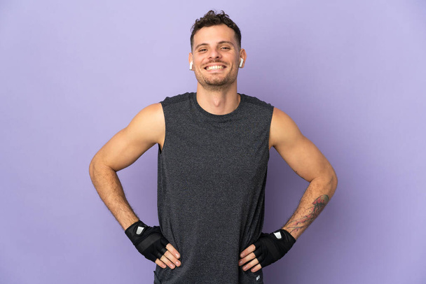 Young caucasian handsome man isolated on purple background posing with arms at hip - Zdjęcie, obraz