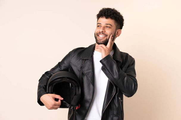 Young Moroccan man with a motorcycle helmet isolated on beige background thinking an idea while looking up - Foto, Imagen