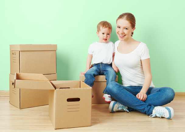 feliz familia madre e hija bebé en un apartamento vacío con cajas de cartón
 - Foto, Imagen