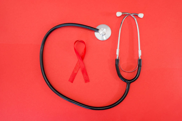 czerwona wstążka i stetoskop na czerwonym tle. 1 grudnia Światowy Dzień AIDS, kampania HIV. - Zdjęcie, obraz