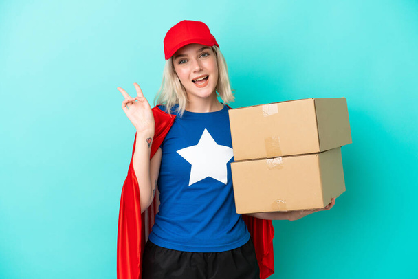 Super Hero caucasian delivery woman isolated on blue background smiling and showing victory sign - Valokuva, kuva