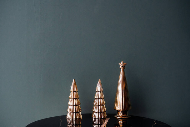 Minimalistic shot of three decorative small Christmas trees of golden color. Decorations for the christmas tree. New Year and Christmas atmosphere. - Photo, Image