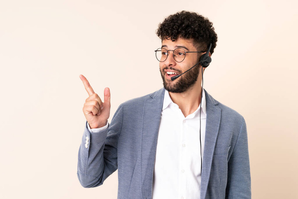 Telemarketer Moroccan man working with a headset isolated on beige background intending to realizes the solution while lifting a finger up - Photo, Image