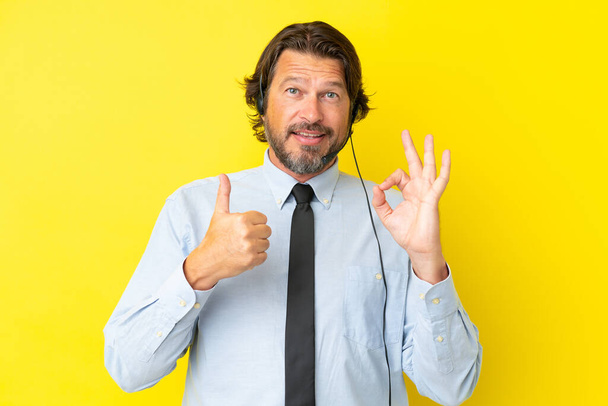 Telemarketer Holanďan pracuje se sluchátky izolované na žlutém pozadí ukazující OK znamení a palec nahoru gesto - Fotografie, Obrázek