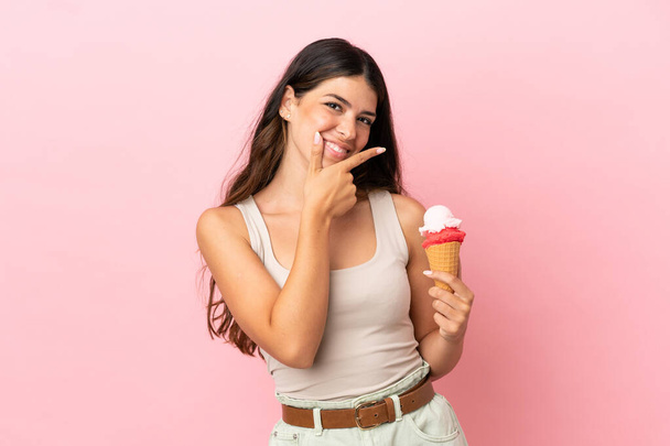Молодая белая женщина с мороженым из корнета на розовом фоне счастливая и улыбающаяся - Фото, изображение