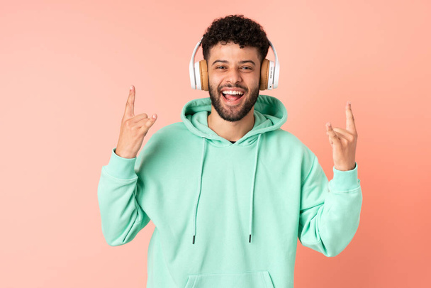 Young Moroccan man isolated on pink background listening music making rock gesture - Foto, immagini