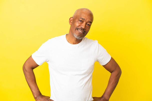 Cubain Senior isolé sur fond jaune posant avec les bras à la hanche et souriant - Photo, image