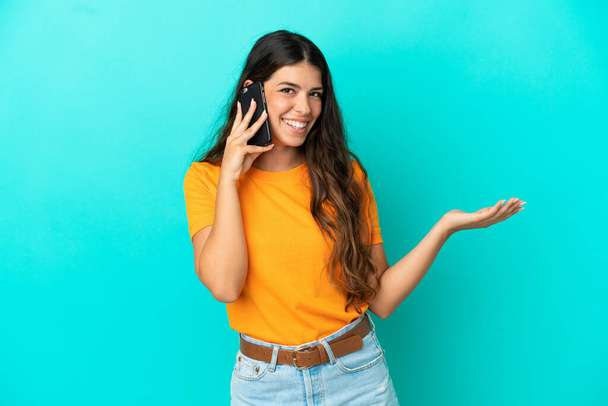 Young caucasian woman isolated on blue background keeping a conversation with the mobile phone with someone - Photo, image