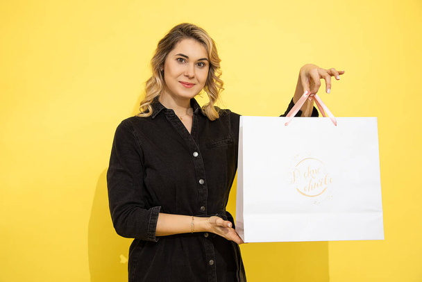 lovely young woman in casual clothing, happy with gift bags, shopping, spring holiday, yellow background, studio shot. Celebrating Woman's Day, birthday, Valentine's, anniversary. Copy space, blank.  - Foto, Bild