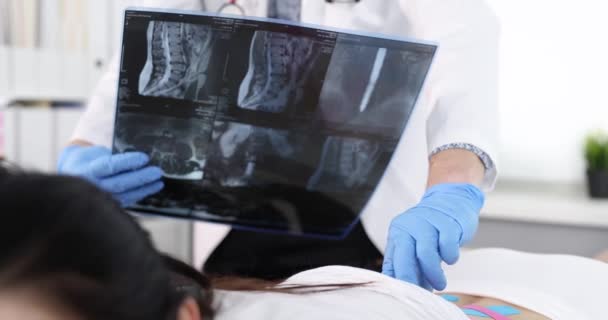 Osteopata palpando processos espinhais de paciente com fitas kinesio e olhando para o raio-x da coluna vertebral filme 4k câmera lenta - Filmagem, Vídeo