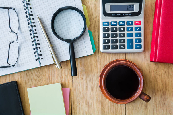 Чашка кофе, ноутбук с ручкой, калькулятор, очки и другие аксессуары на рабочем столе - Фото, изображение