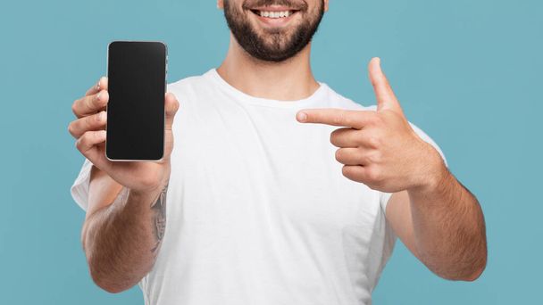 Vrolijke volwassen Europeaan met vinger op smartphone met leeg scherm en beveelt gadget - Foto, afbeelding