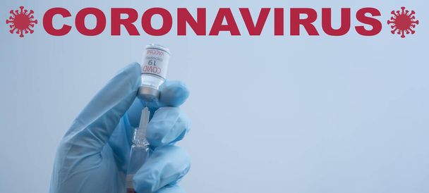CORONAVIRUS COVID-19 / CORONA VACCINATION - zbliżenie od lekarza trzyma w rękach strzykawkę i szczepionkę Corona, izolowane na niebieskim tle z symbolem wirusa - Zdjęcie, obraz