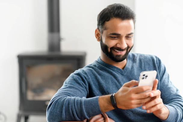 Smiling Indian guy wearing casual outfit messaging, texting on the smartphone - Photo, Image