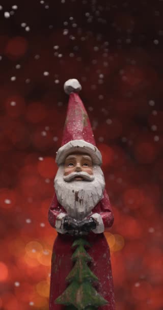 juguete de Navidad de madera que ilustra a Santa Claus de pie frente a las luces rojas fondo bokeh mientras cae nieve - Imágenes, Vídeo