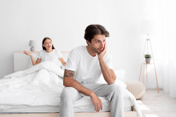 Traurig aufgebracht kaukasischer Millennial Ehemann ignoriert wütende Frau, Dame sitzt im Bett und schreit Mann an - Foto, Bild