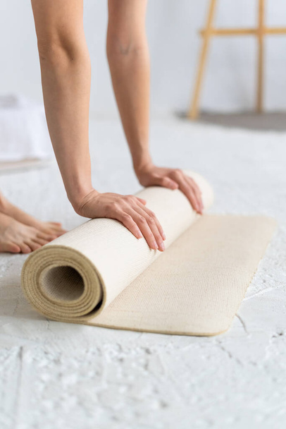 Close-up of female hands rolling out beige yoga mat. Yoga Home. - Foto, Bild