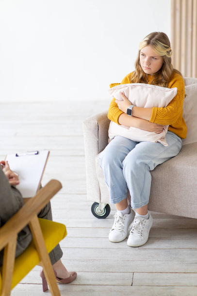 Upset and worried teenage girl sits on couch and hugs pillow. Psychotherapy session. Teenage psychology. - Fotoğraf, Görsel