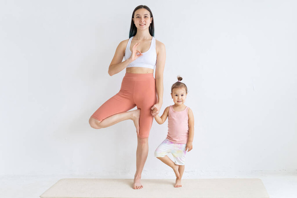 Young attractive mother meditates with her little daughter. Balance exercise. Couple yoga. - Fotó, kép
