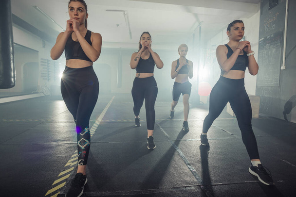 Grupo de deportistas en ropa deportiva haciendo ejercicio de salto en el gimnasio con su pierna izquierda - Foto, Imagen